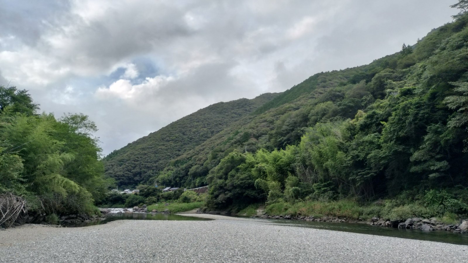 小石の広い河原と、緑の山の間を流れる川。空は曇っている