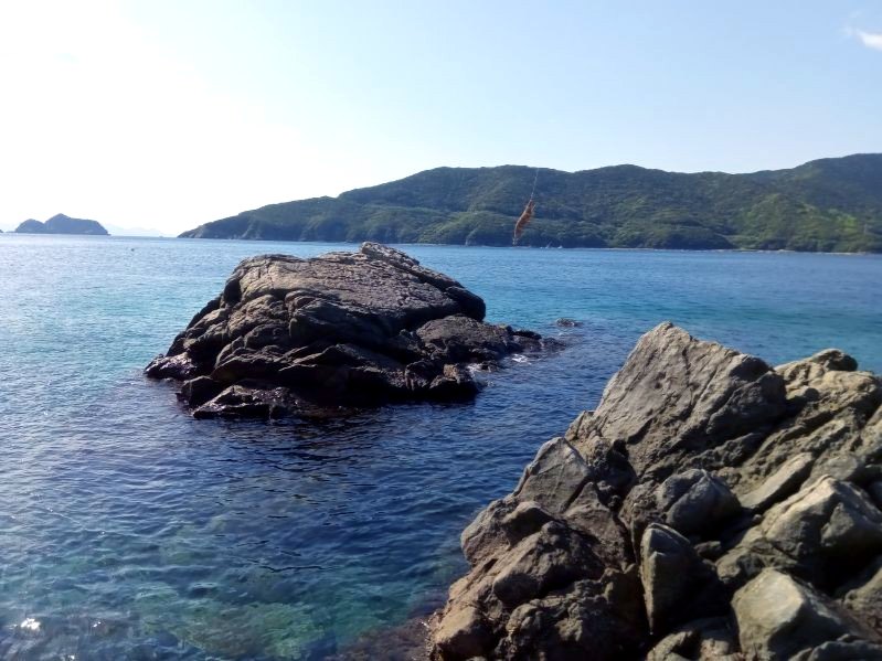 澄んだ海に突き出た岩と、奥に見える緑の山