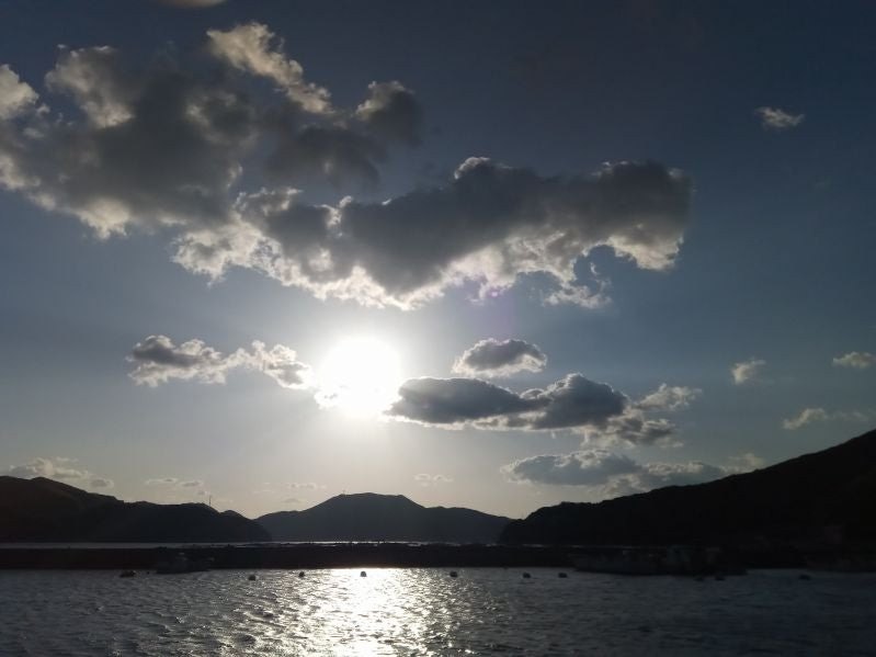 雲の間から差す太陽の光と、光る海面と山の影