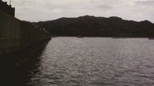 曇り空の下、堤防の脇に広がる穏やかな湾と奥の山並み